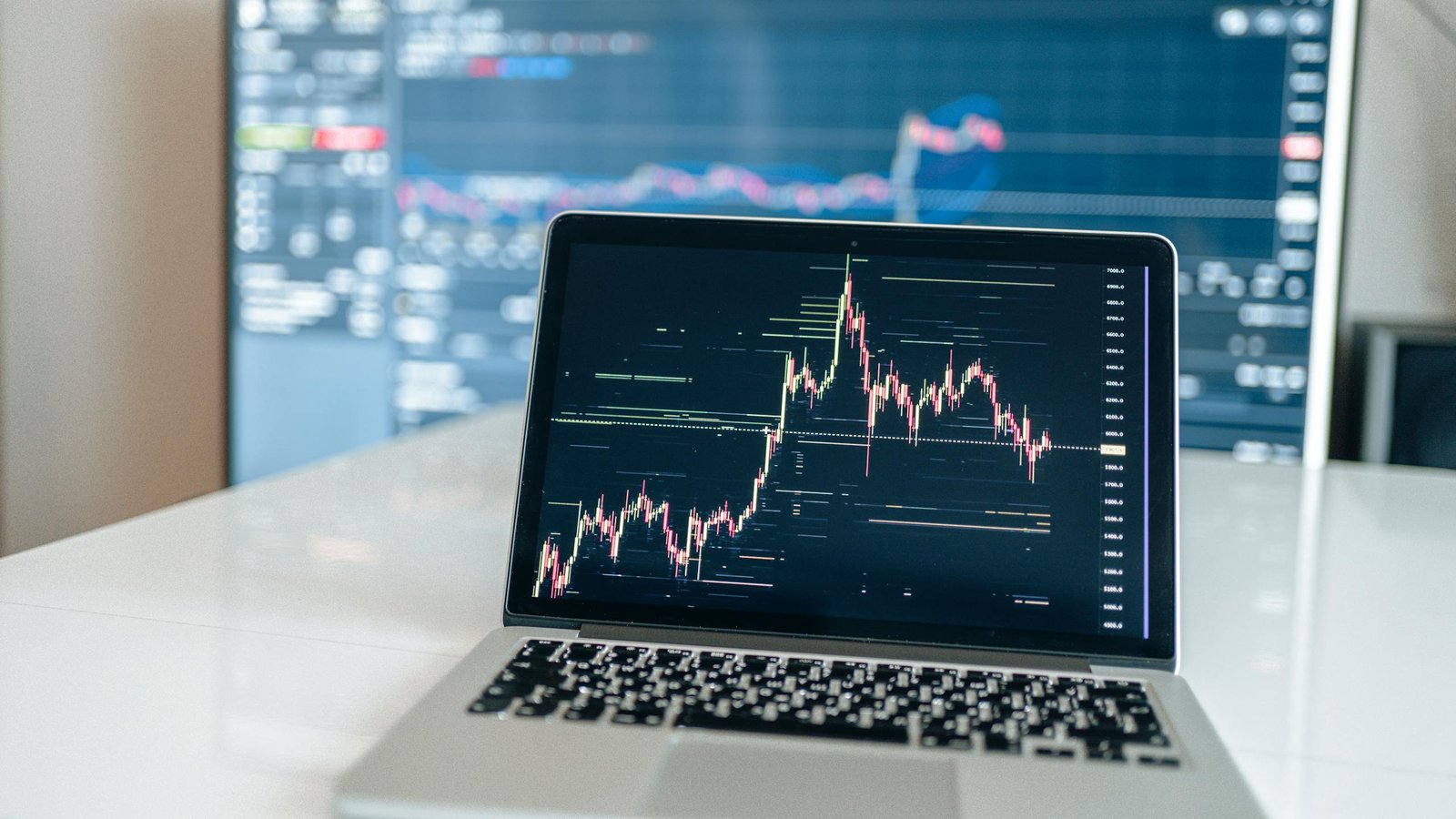 Laptop displaying cryptocurrency trading chart on a white desk.