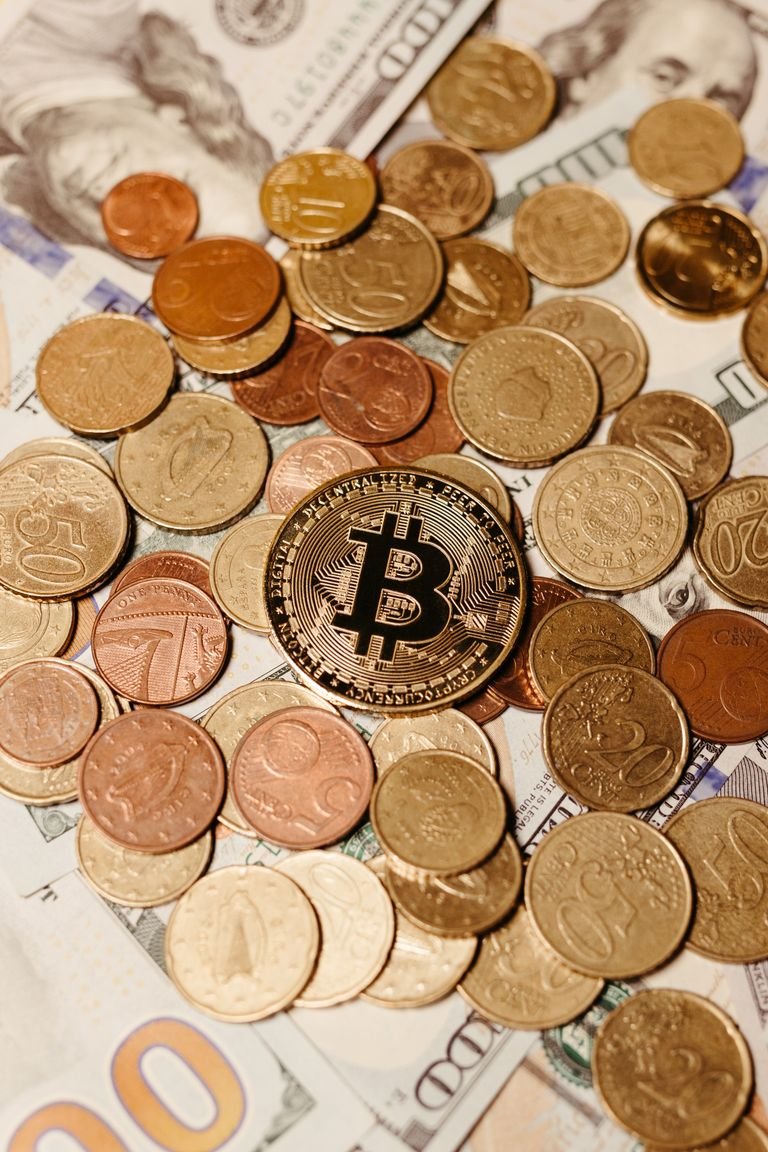 A collection of Bitcoin and various currency coins scattered on US dollar bills, symbolizing digital and traditional currency interplay.