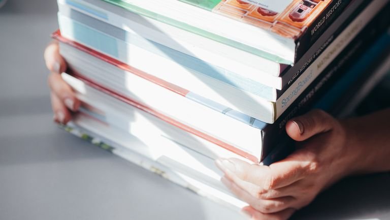 Close-up of hands holding a stack of colorful books in natural light.