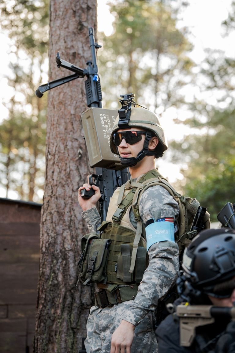 Portrait of a soldier in full uniform and gear standing outdoors with his firearm.