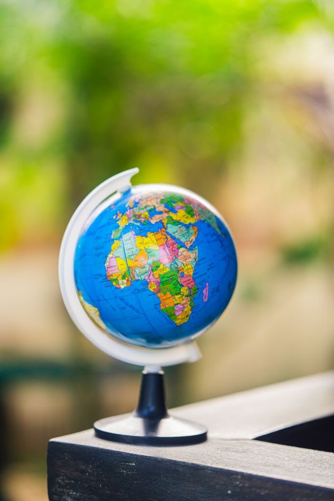 Vibrant miniature globe placed on a table, showcasing continents with blurred green background.